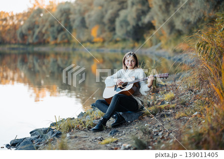 Portrait of a young smiling girl playing the guitar. Beautiful female enjoying nature and playing her favourite instrument Portrait of a young smiling girl playing the guitar. Beautiful female enjoying nature and playing her favourite instrument 139011405