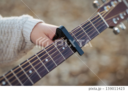 Girl guitarist clinging capo to guitar. Play the guitar using a capo (musical device) 139011423