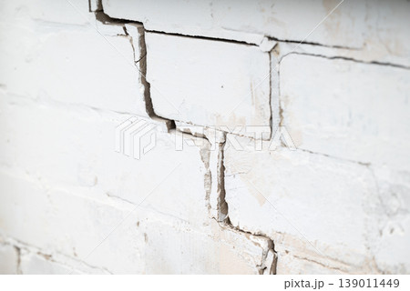 Crack on the white brick wall. Concept of ruining building errors while building structures, deterioration of building 139011449
