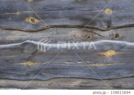 Rustic background of weathered grey wooden planks with prominent knots and wavy edges. Natural aged timber texture with horizontal lines Rustic background of weathered grey wooden planks with prominent knots and wavy edges. Natural aged timber texture with horizontal lines 139011694