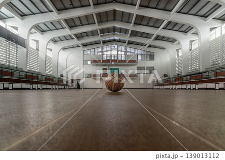 There is a profound stillness in a space designed for noise. Here, white architectural ribs soar toward a vaulted ceiling, framing a lone basketball in a glow of natural light. This low-angle 139013112