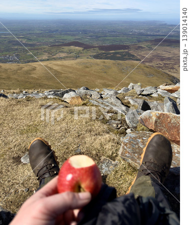Person enjoying apple on mountain top with scenic view Person enjoying apple on mountain top with scenic view 139014140