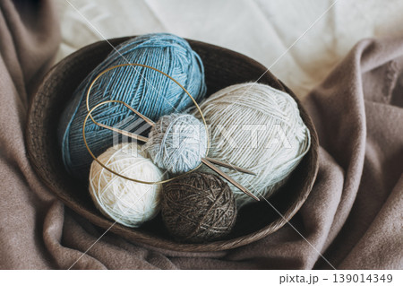 Skeins and balls of woolen yarn and knitting needles for hand knitting in a basket. Natural colors. Skeins and balls of woolen yarn and knitting needles for hand knitting in a basket. Natural colors. 139014349