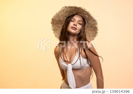 Young woman confidently posing in straw hat and white bikini while ready for summer vacation 139014396