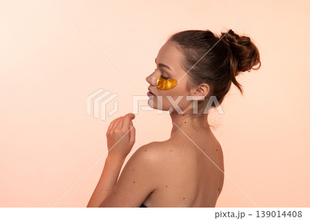 Young woman applying gold eye patches for anti-aging skincare and beauty routine, focusing on self-care and relaxation Young woman applying gold eye patches for anti-aging skincare and beauty routine, focusing on self-care and relaxation 139014408