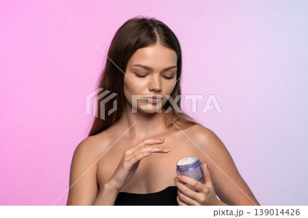 Woman closing eyes while applying a hydrating face cream to her skin, practicing a daily self-care beauty routine 139014426