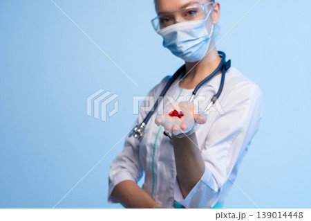 Medical professional wearing protective gear and stethoscope offering red pills, showcasing healthcare and treatment options Medical professional wearing protective gear and stethoscope offering red pills, showcasing healthcare and treatment options 139014448