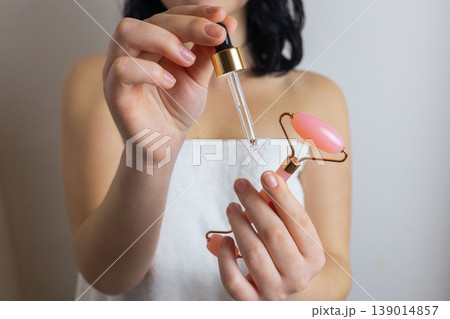 Woman holding facial roller and cosmetic serum dropper during skincare routine, beauty treatment and facial care concept Woman holding facial roller and cosmetic serum dropper during skincare routine, beauty treatment and facial care concept 139014857