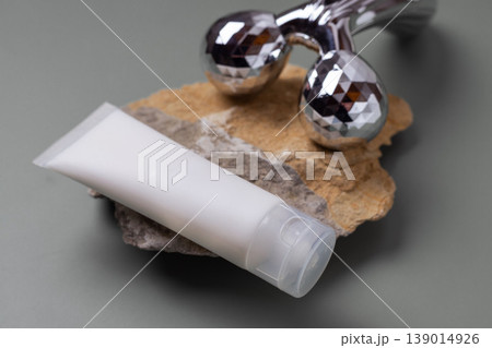 Metal facial roller with moisturizing skincare cream and cosmetic jar on neutral background, beauty treatment concept Metal facial roller with moisturizing skincare cream and cosmetic jar on neutral background, beauty treatment concept 139014926