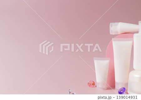 Minimal skincare cosmetic products with lotion tubes and bottles on pink podium with decorative gemstones, beauty product display concept Minimal skincare cosmetic products with lotion tubes and bottles on pink podium with decorative gemstones, beauty product display concept 139014931