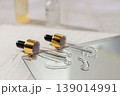 Glass cosmetic droppers with transparent serum on mirror surface, skincare essence drops and reflection, beauty treatment concept, minimalist cosmetic product background. 139014991