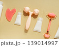 Flat lay skincare beauty routine with cosmetic bottles, serum dropper, facial roller, massage tool and towel on warm pastel background 139014997