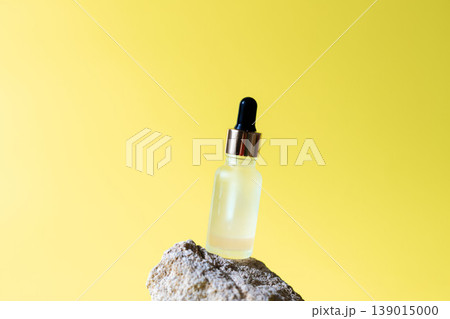 Cosmetic serum dropper bottle on natural stone with bright yellow background, skincare oil beauty product concept Cosmetic serum dropper bottle on natural stone with bright yellow background, skincare oil beauty product concept 139015000