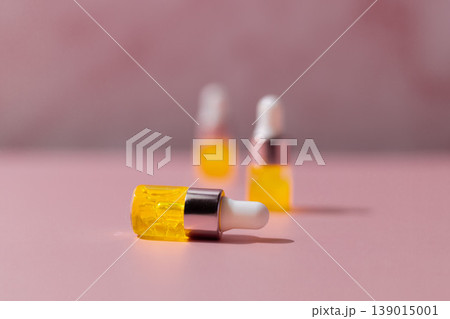Yellow cosmetic serum dropper bottles on pink background, skincare oil texture with pipette, beauty product concept Yellow cosmetic serum dropper bottles on pink background, skincare oil texture with pipette, beauty product concept 139015001