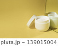 Open cosmetic cream jar with moisturizer reflected in mirror on yellow background in warm sunlight, skincare concept 139015004