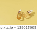 Two cosmetic serum dropper bottles with golden liquid on pastel yellow background in warm sunlight, skincare concept 139015005