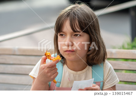 Girl age 7 eats waffle dessert on a bench during a walk. Girl age 7 eats waffle dessert on a bench during a walk. 139015467