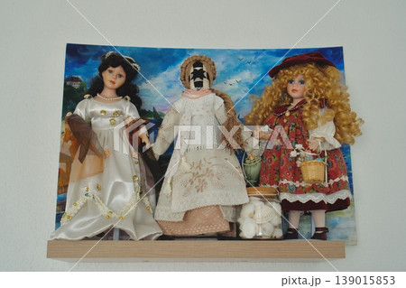 Display of three collectible porcelain dolls on a wooden shelf. Vintage dolls with traditional costumes. Display of three collectible porcelain dolls on a wooden shelf. Vintage dolls with traditional costumes. 139015853