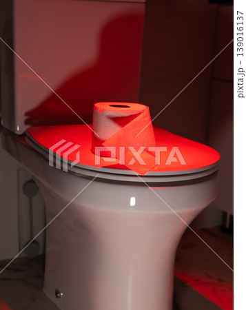 Toilet paper on toilet lid with red light. Symbolic representation of bowel movement issue and digestive health problem. photography Toilet paper on toilet lid with red light. Symbolic representation of bowel movement issue and digestive health problem. photography 139016137