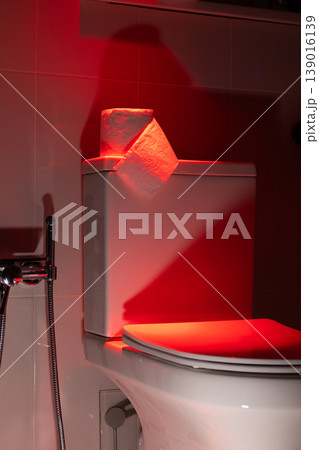 Roll of toilet paper on a white cistern in a dark red light. Conceptual visualization of bowel movement problem, digestive health issue, or gastrointestinal symptom. photography Roll of toilet paper on a white cistern in a dark red light. Conceptual visualization of bowel movement problem, digestive health issue, or gastrointestinal symptom. photography 139016139