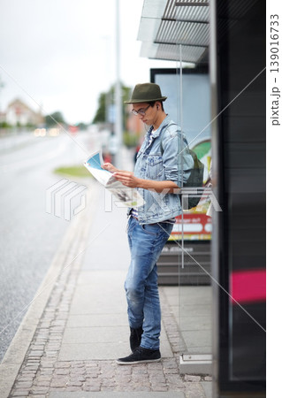 Man, journey and bus stop with map, travel and adventure by commute, transportation and planning for trip. Male person, information and guide for direction, navigation and vacation or earphones 139016733