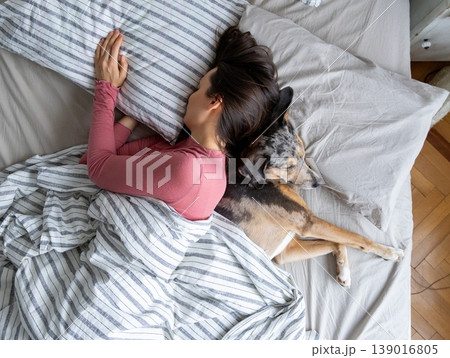 top view of sleeping woman and dog in bed. girl and pet sleep comfortably together and cuddle. top view of sleeping woman and dog in bed. girl and pet sleep comfortably together and cuddle. 139016805