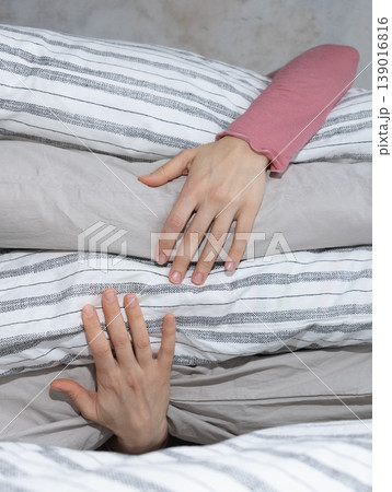 woman holds stack of pillows with her hands while sitting on the bed. rest and restful sleep. woman holds stack of pillows with her hands while sitting on the bed. rest and restful sleep. 139016816