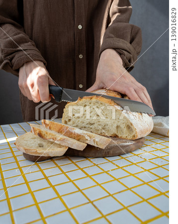 person cuts white bread on wooden board with knife. homemade sourdough bread with crispy crust. person cuts white bread on wooden board with knife. homemade sourdough bread with crispy crust. 139016829