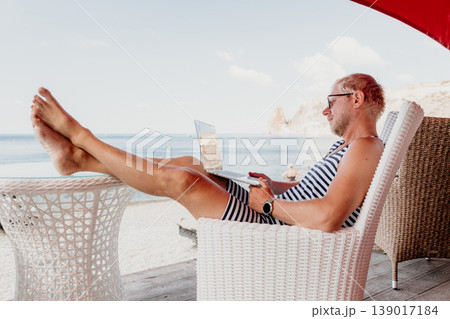 Freelancer laptop beach man working on a computer while relaxing on a seaside terrace representing digital nomad lifestyle and remote office Freelancer laptop beach man working on a computer while relaxing on a seaside terrace representing digital nomad lifestyle and remote office 139017184