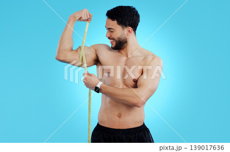 Happy man, measuring tape and bicep in fitness, bodybuilding or weight loss against a blue background. Male person, athlete or bodybuilder smile taking muscle or arm measurement for flex on mockup 139017636