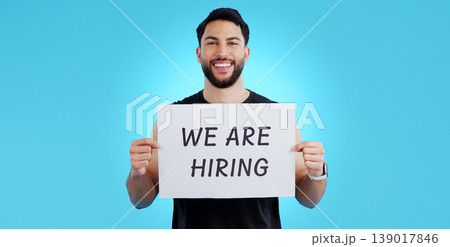 Portrait, smile and man with we are hiring, poster or announcement in studio on blue background. Recruitment, banner and face of male model with news, announcement or business, opportunity or offer Portrait, smile and man with we are hiring, poster or announcement in studio on blue background. Recruitment, banner and face of male model with news, announcement or business, opportunity or offer 139017846