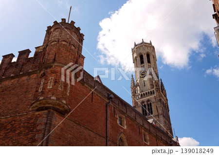 Sunny view of the Belfry of Bruges rising above the historic Markt square, showcasing medieval Flemish architecture under a clear blue sky, Brugge, West Flanders, Belgium 139018249