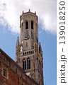 Sunny view of the Belfry of Bruges rising above the historic Markt square, showcasing medieval Flemish architecture under a clear blue sky, Brugge, West Flanders, Belgium 139018250