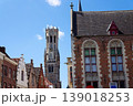 Sunny view of the Belfry of Bruges rising above the historic Markt square, showcasing medieval Flemish architecture under a clear blue sky, Brugge, West Flanders, Belgium 139018253