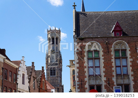 Sunny view of the Belfry of Bruges rising above the historic Markt square, showcasing medieval Flemish architecture under a clear blue sky, Brugge, West Flanders, Belgium 139018253