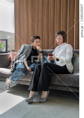 Businesswomen holding notepad brainstorming and discussing together sitting on sofa at office. Brainstorm, notepad, business, teamwork, office. 139020007