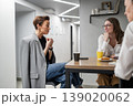 Businesswomen discussing work at kitchen table with drinks and snacks in modern office. Discussion, kitchen, drinks, snacks, teamwork, businesswomen. 139020062