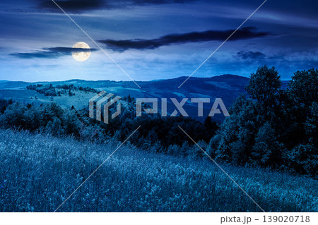 mountainous countryside landscape in summer at night. full moon over grassy field on a hillside. view of a forested mountain ridge in the distance. mysterious weather with cloudy sky mountainous countryside landscape in summer at night. full moon over grassy field on a hillside. view of a forested mountain ridge in the distance. mysterious weather with cloudy sky 139020718