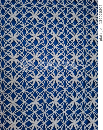 A detailed view shows handmade Yelets white bobbin lace placed against blue fabric. This arrangement highlights the skill involved in crafting lace patterns with fine threads. 139020802