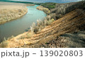 A river runs under a steep bank in a natural landscape. Trees line the river, and a forest is visible in the background. The scene is bright and shows a clear sky. 139020803