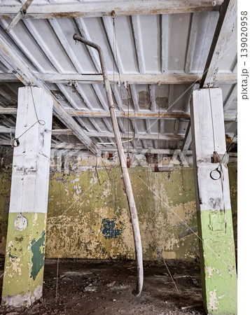 The interior of an abandoned tobacco factory in Yelets shows peeling green paint on pillars. A rusty pipe hangs from the ceiling, revealing the decay of the once busy space. The interior of an abandoned tobacco factory in Yelets shows peeling green paint on pillars. A rusty pipe hangs from the ceiling, revealing the decay of the once busy space. 139020958