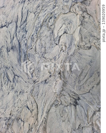 Swirling dark minerals create natural designs in light beach sand where the tide has just gone out. The shoreline reveals intricate patterns formed by water and land. 139020959