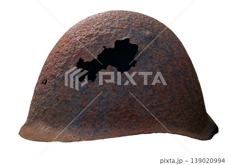 An antique soldier helmet from World War II shows a shell hole. It is isolated against a plain background, highlighting its aged metal and history. An antique soldier helmet from World War II shows a shell hole. It is isolated against a plain background, highlighting its aged metal and history. 139020994