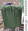 The thick, textured green bristles of a plastic garden broom are displayed on a shelf in a retail store. Bright lighting shows the details of the bristles. 139020998