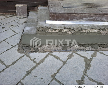 A close view shows a worker applying fresh cement mortar to repair concrete stairs. The area has uneven surfaces and requires maintenance for safety. The renovation is part of home improvement. A close view shows a worker applying fresh cement mortar to repair concrete stairs. The area has uneven surfaces and requires maintenance for safety. The renovation is part of home improvement. 139021012