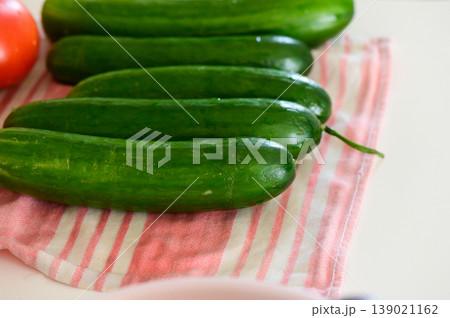 Fresh cucumbers arranged on a pink striped kitchen towel, ready for a delicious summer salad preparation 139021162