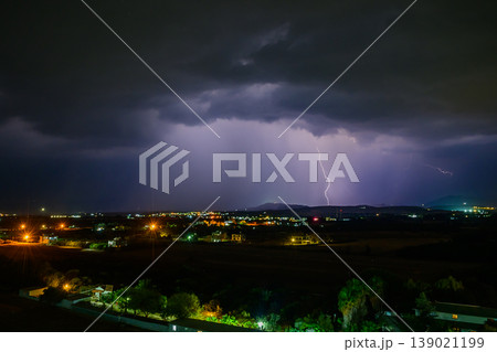 Majestic lightning illuminates a tranquil town under stormy skies at night Majestic lightning illuminates a tranquil town under stormy skies at night 139021199