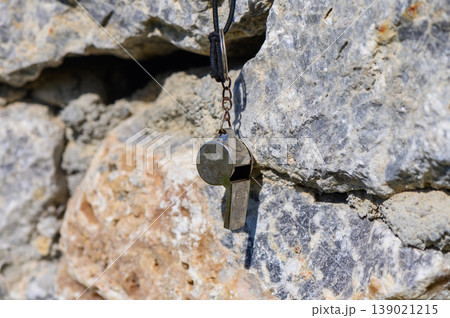 A silver whistle hanging from a rocky wall in bright sunlight during a serene afternoon adventure 139021215