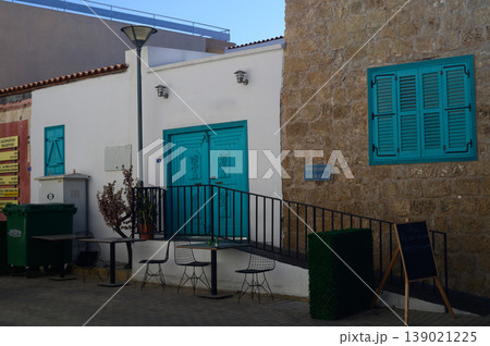 Charming coastal building with turquoise doors and outdoor seating in a Mediterranean village bathed in sunlight 139021225