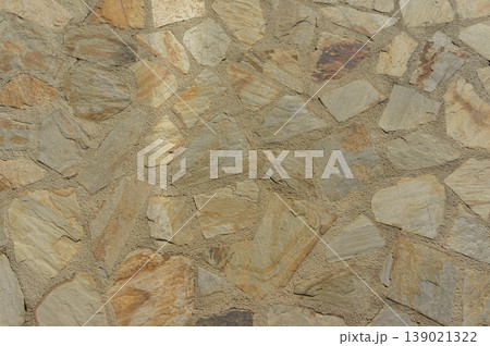 Textured stone wall with a natural color palette showcasing earthy tones and rustic charm in bright daylight Textured stone wall with a natural color palette showcasing earthy tones and rustic charm in bright daylight 139021322
